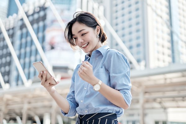 A beautiful Asian business woman is looking at her smartphone and very happy.